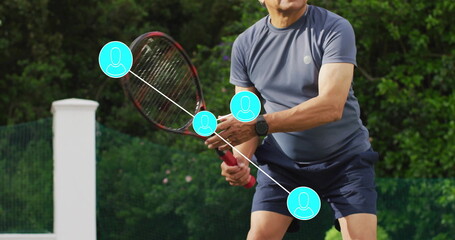 Gripping senior man in sportswear performing backhand on tennis court, with smartwatch and net post
