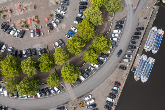 Aerial view of cars neatly parked in designated spots near the waterfront, accentuated by vibrant green trees and boats docked nearby, Gothenburg, Vastra Gotaland, Sweden.