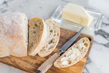 Sliced ciabatta bread with fresh butter on a wooden cutting board. marble background. top view