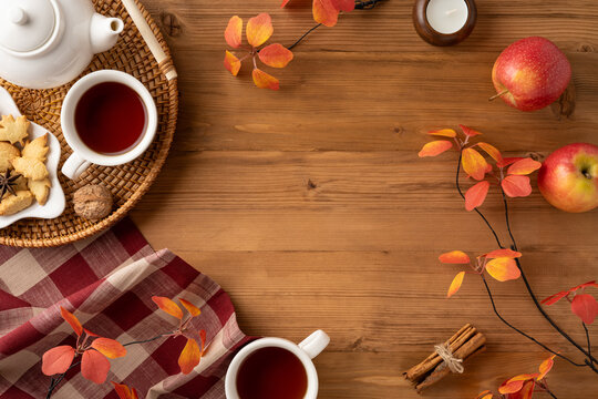 Cozy autumn thematic setup featuring tea, cookies, apples, and fall leaves on a wooden surface