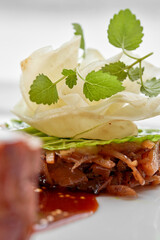 A creative gourmet dish with a piece of meat, a red sauce, and a side of vegetable tartare topped with a delicate flower petal on a white plate.
