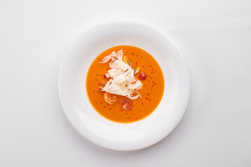 A vibrant pumpkin cream soup with shrimp and a delicate garnish of fresh white vegetable ribbons, served in a white bowl.