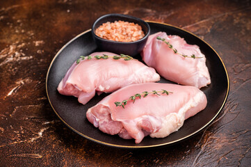 Raw Chicken thigh fillet meat, Skinless boneless poultry meat on a plate. brown background. top view