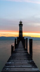 Obraz premium Wooden pier extending to a lighthouse at sunset over calm water