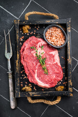 Marbled raw Rib eye steak with herbs in wooden tray, fresh beef meat. black kitchen background. top view