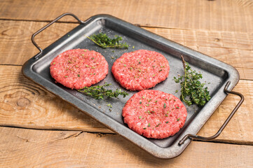 Raw hamburger minced meat patties  for burgers with herbs on tray. wooden background. top view