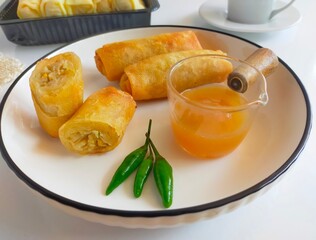 A plate of delicious Lumpia Semarang, a popular traditional spring roll from Semarang, Indonesia. The crispy deep-fried spring rolls are served with a sweet and sour sauce and fresh green chili.