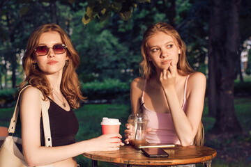 Two young women enjoying a sunny day at a park cafe while sipping drinks and chatting in the afternoon
