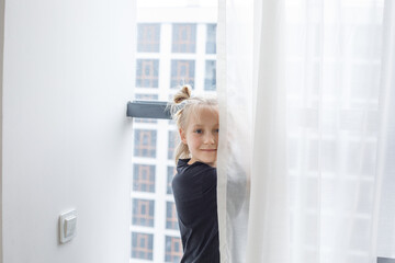 Smiling child girl standing at the window at home