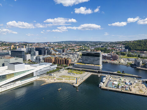 Aerial view of the Oslo Opera House's white angles contrasting with the deep blue fjord and the city's modern architecture under a clear sky, Oslo, Oslo, Norway.