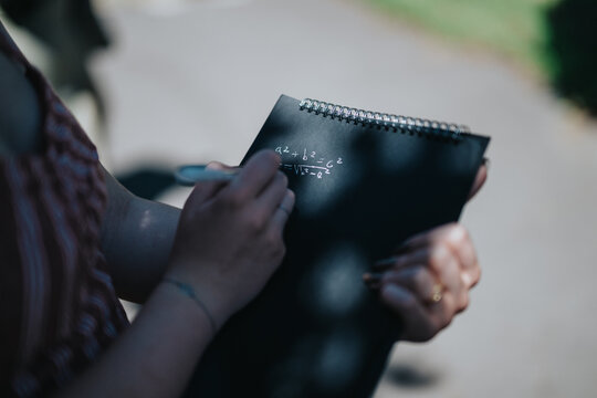 A student writes mathematical equations on a notebook during an outdoor educational activity.