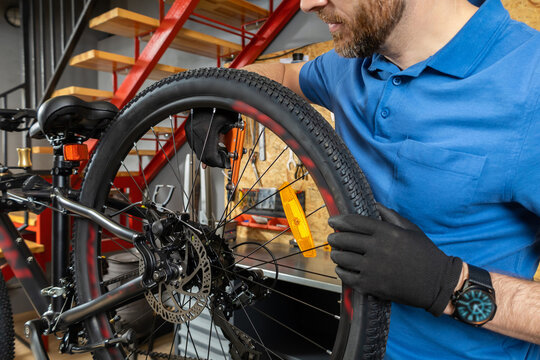 Young man in blue polo and beanie fixing bike wheel in modern workshop - Powered by Adobe