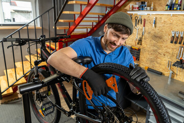 Bearded man in blue polo tuning bike wheel in workshop