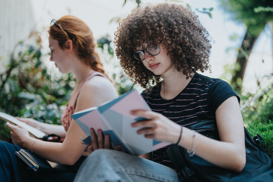 Two young students engage in reading together outdoors in a peaceful environment surrounded by greenery. Their focus and the natural setting reflect a serene moment of learning and relaxation.