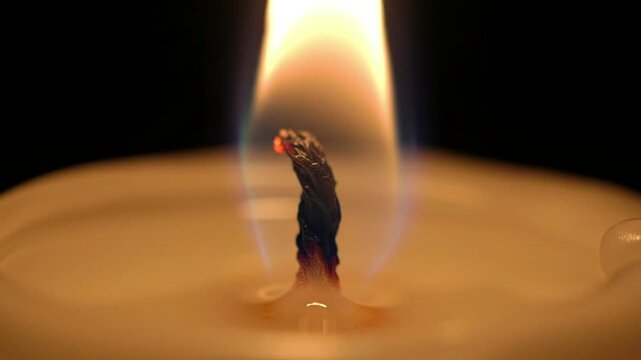 Closeup of a burning candle wick with a bright flame against a dark backdrop