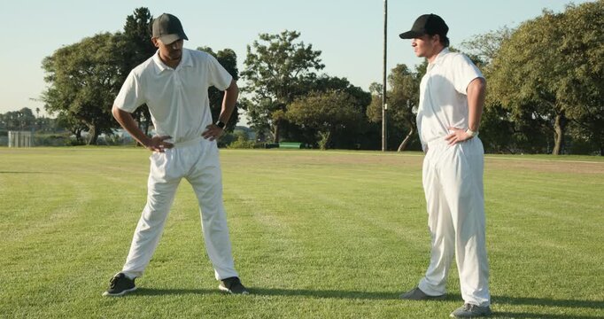 Diverse male teammates gesturing before stretching in white uniforms on cricket ground warming up - Powered by Adobe