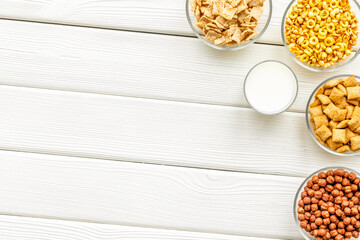 Various corn cereals in bowls and milk on white wooden background top view copyspace