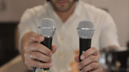 Close-up of a person's hands holding two professional dynamic microphones, symbolizing sound recording, live performance, broadcasting, or public s...