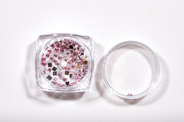accesorios cuadrados color rosa para decorar de uñas en una cajita transparente sobre fondo blanco