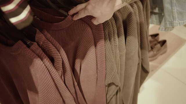 Hand choosing knit sweaters on clothing rack in store