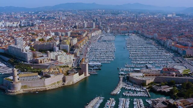 4K drone over Marseille&rsquo;s Vieux-Port : dense yacht marina flanked by Fort Saint-Jean and Fort Saint-Nicolas, historic waterfront and city skyline with Provencal hills beyond.
