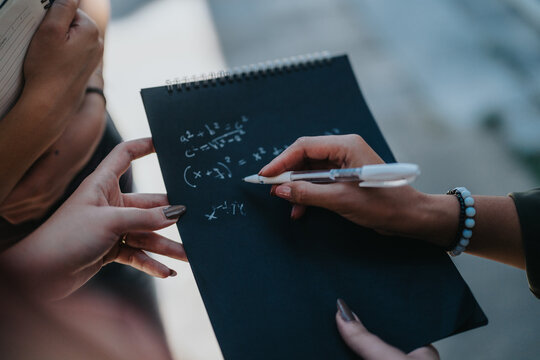 A group of students engaging in solving mathematical equations on a notebook outdoors, showcasing teamwork, education, and collaborative learning in a casual environment. - Powered by Adobe