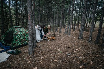 Friends bonding outdoors in nature with a dog near a tent and trees