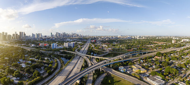 Aerial view of a sprawling highway interchange, a network of concrete veins amidst the vibrant greenery, leading to the gleaming skyline, Miami, Florida, United States.