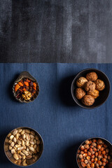 Bowls with nuts and blue table cloth on black chalkboard background. Flat lay. Top view.