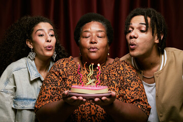 Portrait of middle aged Black woman holding birthday cake with lit candles, while biracial young...