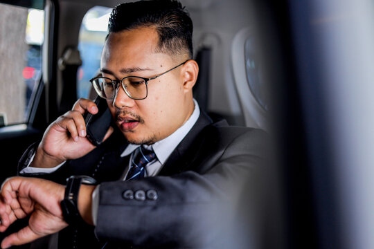 Businessman In Suit Multitasking In A Car, Checking Smart Watch While On A Phone Call