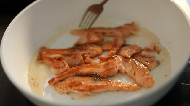 A woman cooks fresh salmon fillets in a skillet on her home kitchen stove, preparing a delicious and healthy meal for lunch.
