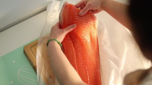 A woman in her home kitchen unwraps fresh salmon fillets, preparing ingredients for a healthy and delicious homemade meal.