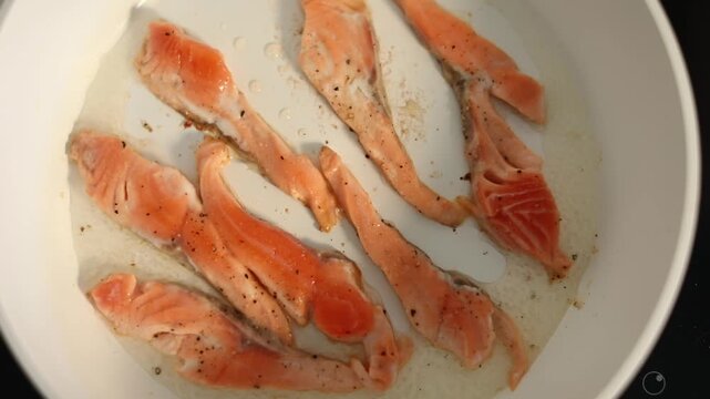 A woman cooks fresh salmon fillets in a skillet on her home kitchen stove, preparing a delicious and healthy meal for lunch.