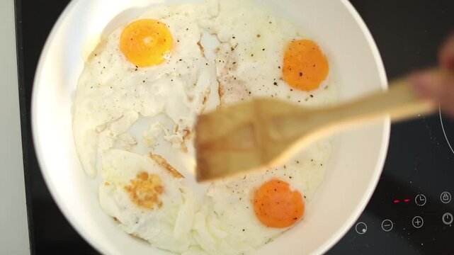 A woman fries fresh eggs in a skillet on her home kitchen stove, preparing a simple and delicious breakfast