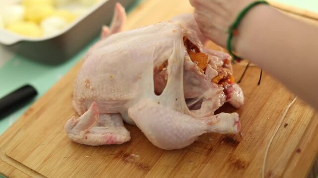A woman is preparing a meal by carefully stuffing a whole chicken in her kitchen. The video shows the step-by-step process of home cooking, creating a cozy and appetizing atmosphere.