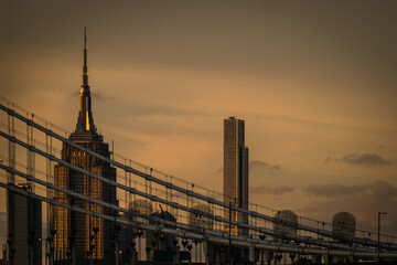 View of the iconic Empire State Building piercing the dusky sky, framed by the intricate cables of a bridge, capturing the essence of urban grandeur, New York, New York, United States.