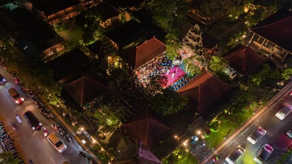 Aerial night view of central Ubud, Bali, with busy street traffic and traditional cultural performance on open-air stage, illuminated by vibrant lights and surrounded by tropical gardens.