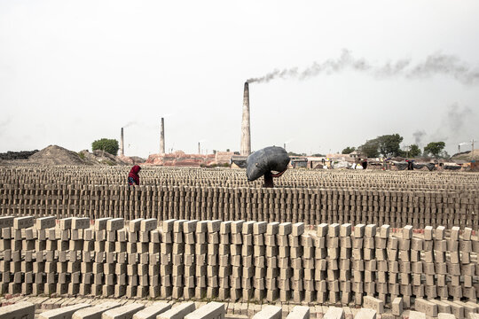 Munshiganj, Bangladesh - 23 November 2024: View of laborers amidst endless rows of drying bricks, with smoke billowing from the towering brick kilns.