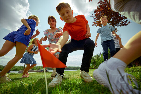 Children energetically engage in a game of capture the flag beneath a bright sky. Concept of childhood competition, active outdoor play, summer group activities