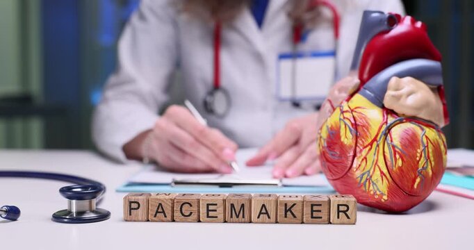 A medical professional studies a pacemaker, taking notes next to an anatomical heart model for education