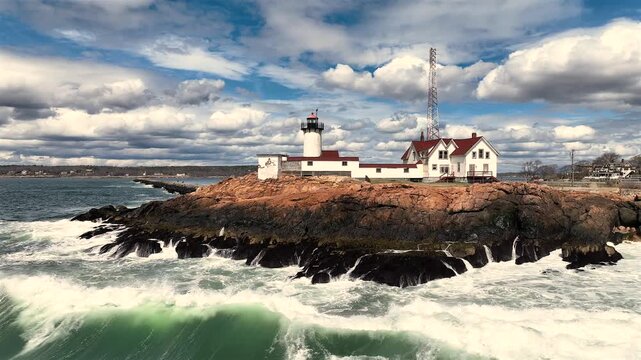 Aerial view of the iconic Eastern Point Light standing proudly against crashing waves and dramatic skies, a beacon of maritime history, Gloucester, Massachusetts, United States.