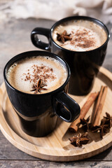 Chai Latte in Black Mug with Spices( star anise and cinnamon) on wooden table