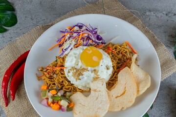 Traditional Indonesian Fried Noodles with Egg Served on White Plate with Pickles and Crackers