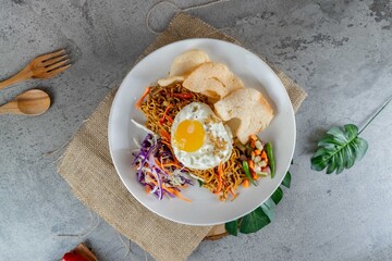 Traditional Indonesian Fried Noodles with Egg Served on White Plate with Pickles and Crackers