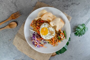 Traditional Indonesian Fried Noodles with Egg Served on White Plate with Pickles and Crackers