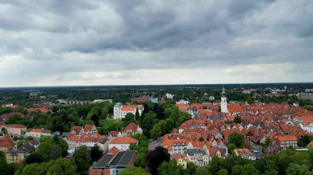 Aerial view of Celle's orange rooftops contrasting with the verdant trees, the white castle, and church under a dramatic sky, Celle, Lower Saxony, Germany.