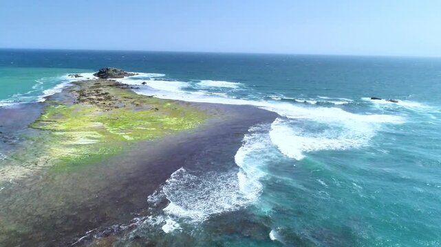Drone aerial footage showing a small tropical island surrounded by turquoise sea, clear shallow water, and gentle waves under bright sunny weather. Perfect for travel, nature, and coastal landscape.