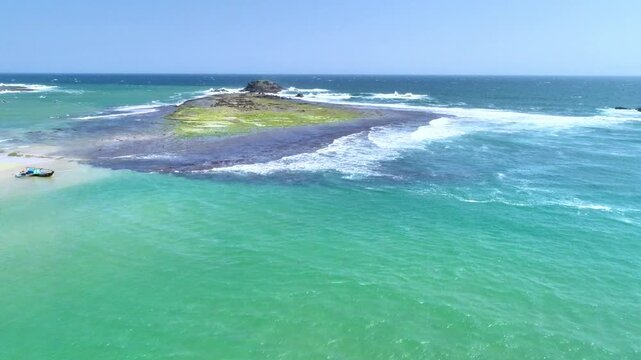 Aerial View of Small Island with Turquoise Sea and Waves in Tropical Coastline. Drone aerial view of a small tropical island with turquoise sea, clear shallow water, and ocean waves under bright sunny