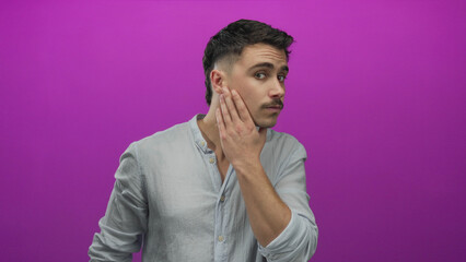 Young hispanic man with short hairstyle touching his face and hair while standing in front of a vibrant isolated pink wall.